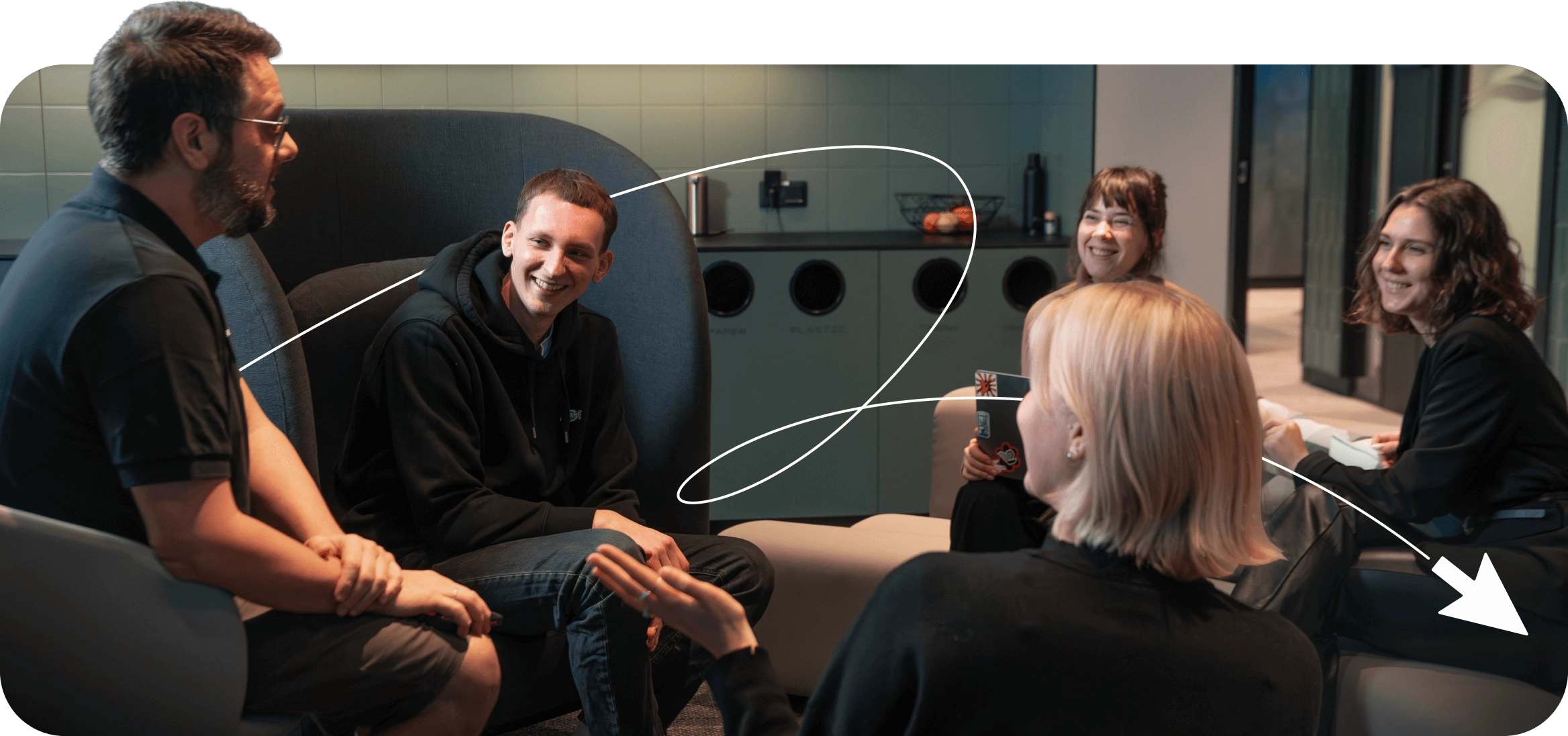Three women and two men sitting in a circle chatting in a modern office lounge.