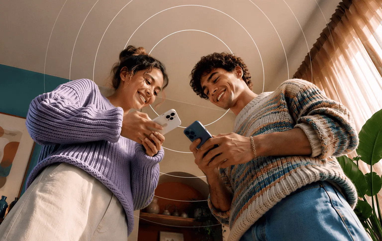 A smiling man and woman in sweaters stand side-by-side, each holding a smartphone beneath a graphic of concentric circles.