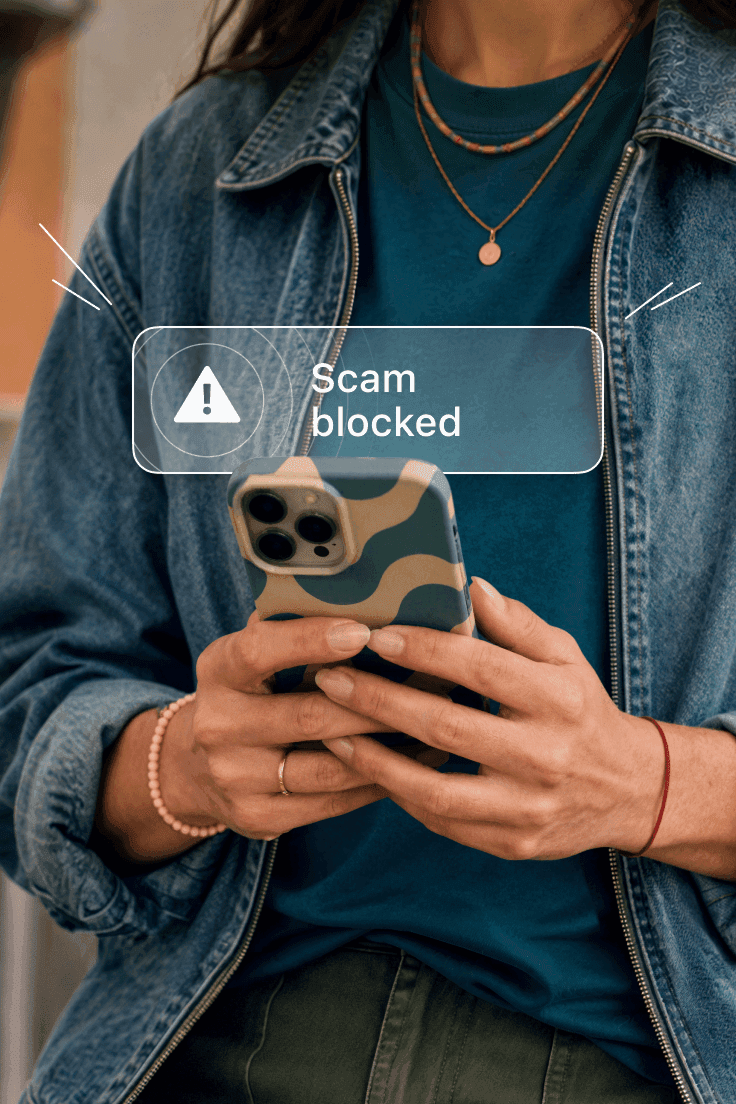 Person holding a smartphone with a Scam blocked notification alert on the screen.