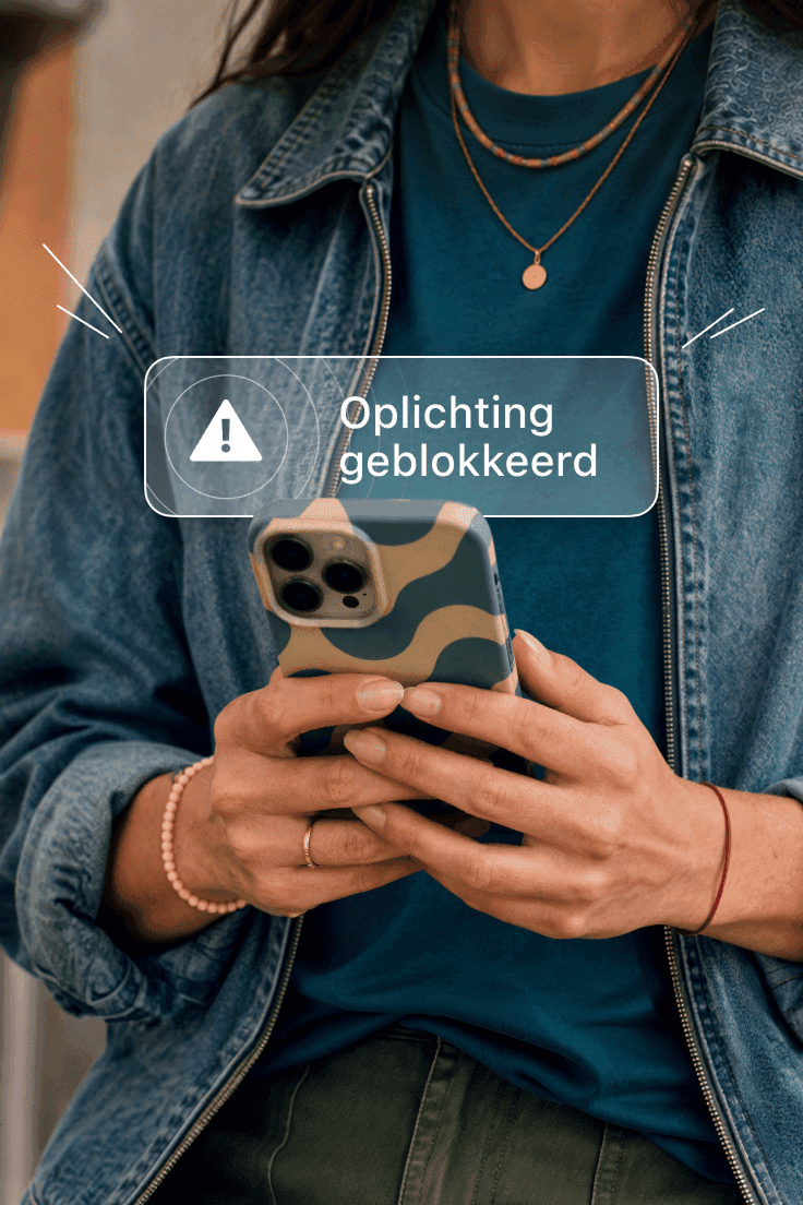 Persoon die een smartphone vasthoudt met de waarschuwing 'Oplichting geblokkeerd' op het scherm.