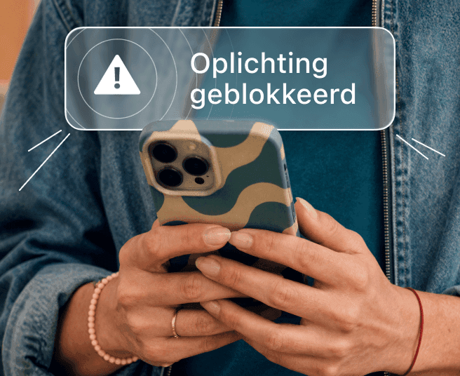 Persoon die een smartphone vasthoudt met de waarschuwing 'Oplichting geblokkeerd' op het scherm.