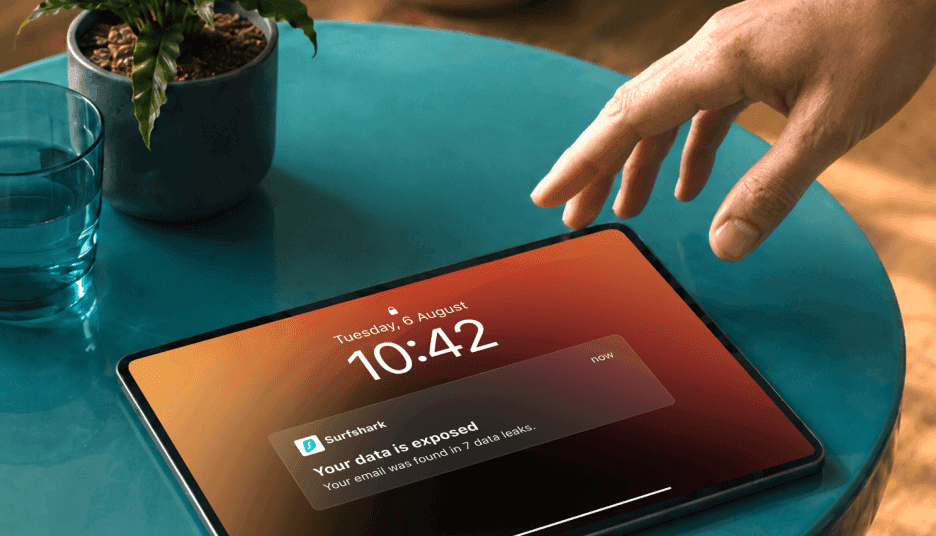 A hand reaching for a tablet displaying a notification that reads Your data is exposed.