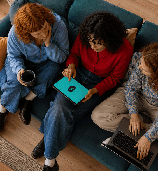 Three people sit on a couch, looking at a tablet screen displaying the Surfshark logo.