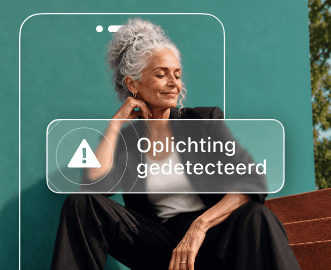 Een vrouw met grijs haar zit tegen een blauwgroene muur, deels verborgen door een telefoonomtrek die een waarschuwing 'Oplichting gedetecteerd' toont.